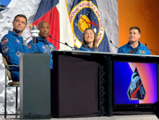 Three men and a woman, all in blue flight suits, sit at a desk during a press conference