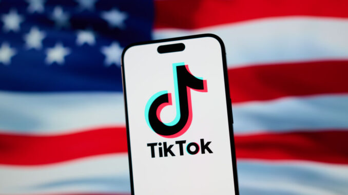 The TikTok app and logo are seen on a mobile device in front of a US flag