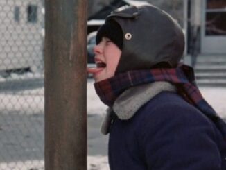 young boy in winter gear, hat and scarf with his tongue sticking out and frozen to a metal pole