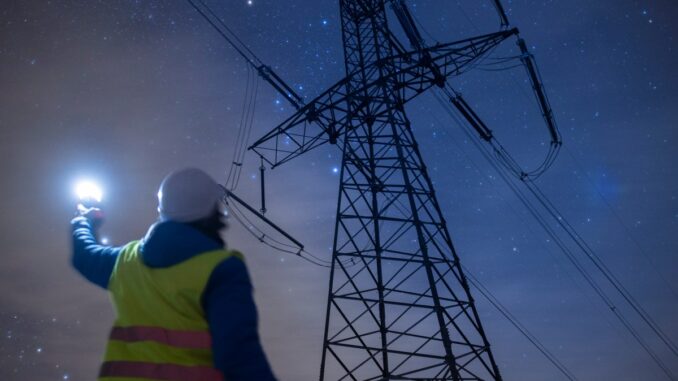 High-voltage engineer working on power lines at night.