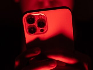 a person holding an iPhone facing the camera in a red backdrop