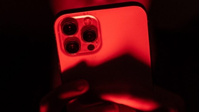 a person holding an iPhone facing the camera in a red backdrop