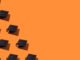 Pattern of black graduation caps with gold tassel with hard shadow, on the left side, on orange background