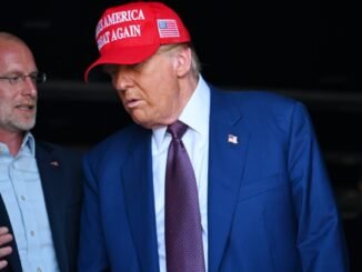 FCC Commissioner Brendan Carr standing next to and speaking to Donald Trump, who is wearing a "Make America Great Again" hat.