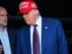 FCC Commissioner Brendan Carr standing next to and speaking to Donald Trump, who is wearing a "Make America Great Again" hat.