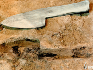 Image of a stone block with the imprint of a device with a blade and handle, with a model of a wooden version of the object that formed it just above.